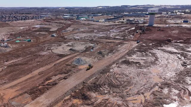 Heavy machinery operates on a sprawling construction site in Erin, with visible earthworks and a water tower. Suitable for infrastructure and urban development themes.