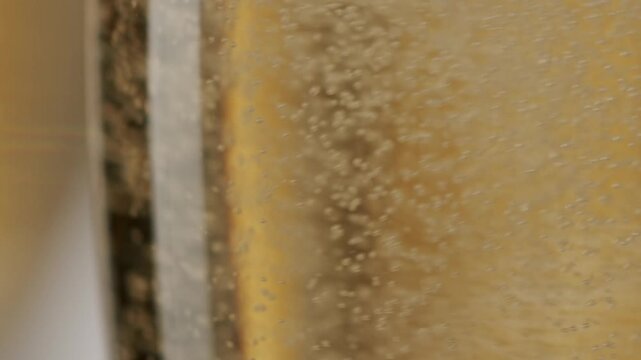 Extreme close-up of sparkling golden wine in a flute with fizzy bubbles rising to the surface in slow motion, creating a celebratory and luxurious background for special occasions.