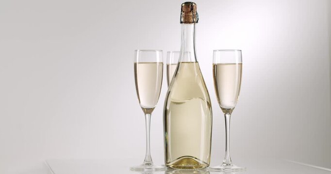 One bottle of sparkling white wine and three full glasses rotating on a reflective surface, offering a detailed view of the elegant setup on an isolated white background for celebratory occasions
