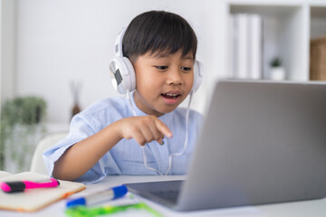 Excited asian boy wearing headphones pointing at laptop screen, Concept of interactive online learning, successful e-learning education, happy student engagement and modern homeschooling concept © Art_Photo