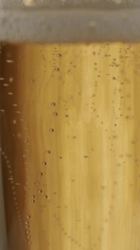 Extreme close-up of golden champagne with effervescent bubbles rising to the surface in a continuous flow, representing celebration, luxury, and festive occasions in slow motion, vertical