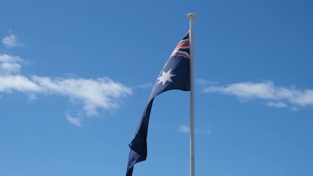 Australian National Flag draped listlessly on a flagpole, barely fluttering due to a weak, stagnant breeze. Sluggish atmosphere and visual metaphor of national fatigue, economic recession, stagnation