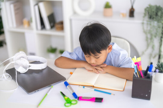 Bored asian student resting chin on hands showing heavy study fatigue, Tired child experiencing homework frustration, Educational burnout and child stress concept for modern mental health problems
