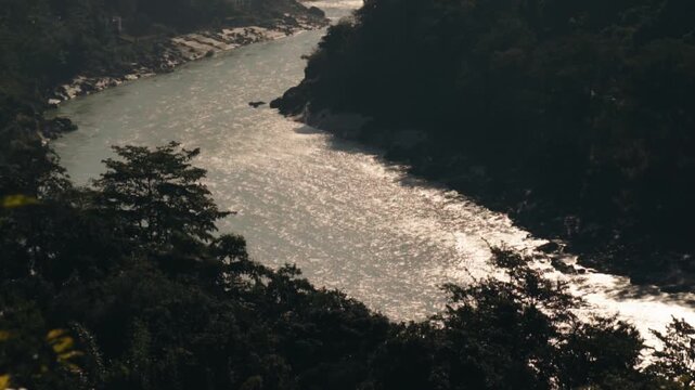 High angle view of a beautiful river flowing through a lush green canyon with sunlight reflecting on the water surface, creating a sparkling and serene natural landscape in the wilderness