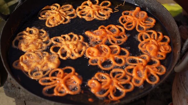 View of traditional jalebi sweets being deep-fried in a large pan of bubbling oil at a street food stall in Nepal.