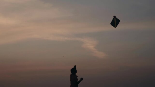 Beautiful silhouette of a young boy happily flying a kite in the evening sky, representing freedom, childhood memories, and the simple joys of outdoor activities and traditional games