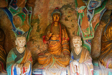 Obraz premium Golden Buddha statue with two disciples in a rock cave sanctuary at the suspended temple Xuankong Si near Mount Heng, Datong, Shanxi, China