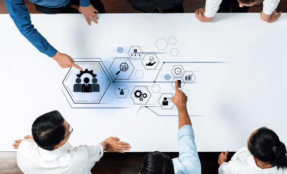 A group of professionals engages in a collaborative meeting over a table, illustrating business concepts with innovative graphics and icons that symbolize teamwork and strategy. Trope