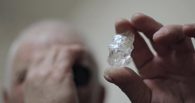 Slow motion closeup of man examining rough crystal gemstone indoors.
