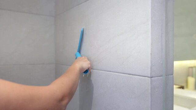 Person Using Blue Squeegee to Clean Glass Shower Door in Bathroom