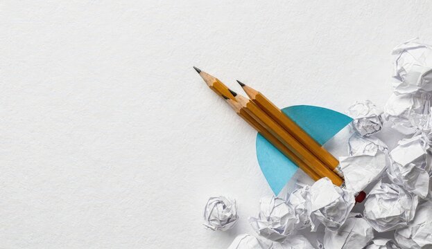 Pencils and paper on a workspace with crumpled paper scraps scattered around