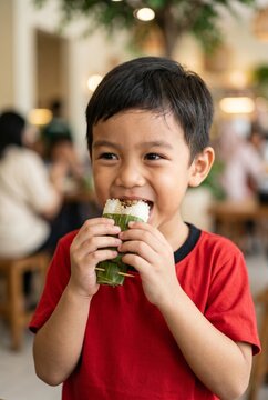 A happy young boy in a red shirt enjoying a traditional Asian rice snack.