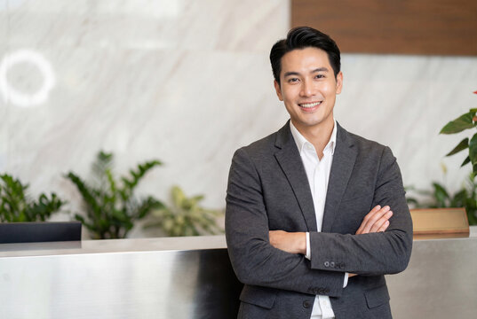 Friendly asian male receptionist standing at a hotel reception desk