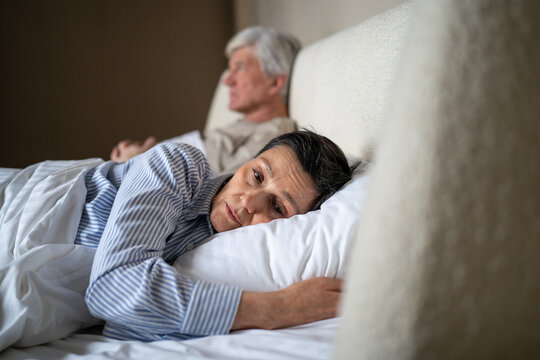 Upset offended elderly wife avoiding contact with husband while lying together in bed in bedroom after quarrel, senior married couple in mental confrontation, aged partners relationships psychology.