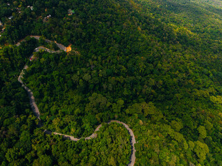 Fototapeta premium Winding road snaking through dense forest from above, travel trip to Thailand concept