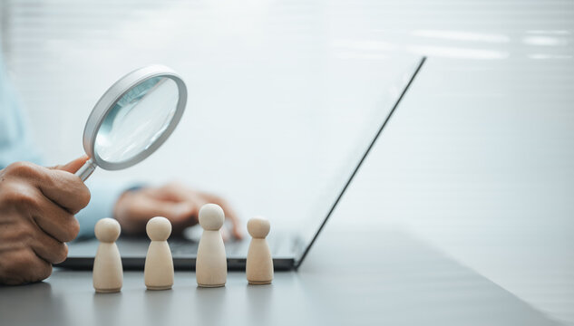 Human resources recruitment and candidate selection concept with magnifying glass, employee figures, and digital hiring process on laptop.