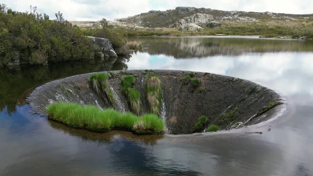 Aerial drone footage of Cov&atilde;o dos Conchos, Portugal: mountain lake with a unique circular spillway surrounded by Serra da Estrela landscape. Ideal for travel and nature projects.