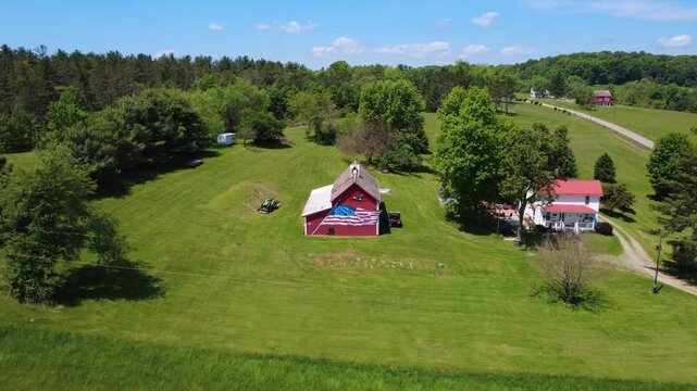 Drone aerial wide shot push across toward a rural farm field into a red barn painted with a patriotic American flag on its front located in Hocking County Ohio