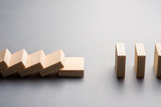 Wooden domino blocks stop before full collapse due to a missing link, symbolizing risk containment, system protection, disruption, resilience, and controlled failure in business or operations