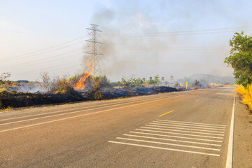 Fototapeta premium Roadside grass fire with smoke pollution near rural highway and power lines