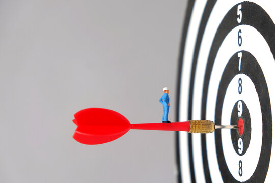 Business Target Achievement and Precision Strategy Concept. Miniature worker standing on a red dart hitting the target board, representing business goals, strategic focus, accuracy, and successful exe