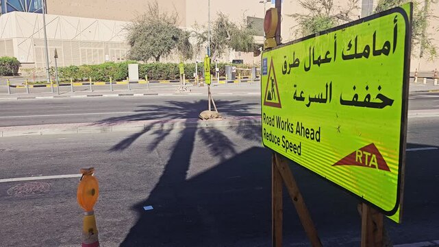Roadworks ahead sign on a sunny street in Dubai. Bright green RTA traffic sign warns drivers to reduce speed near a construction zone.