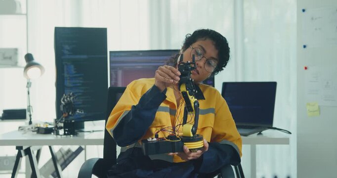 Young African American female robotics engineer discussing mechanical part on video call and looking at camera in laboratory. Remote work, virtual training, online meeting, future technology concept.