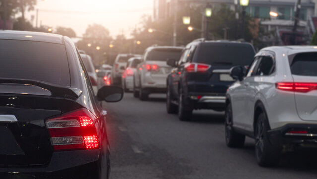 ฺBehind cars stuck in heavy evening traffic as dusk sets in. Red brake lights illuminate the congested city street creating a classic urban rush hour scene under a warm sky.