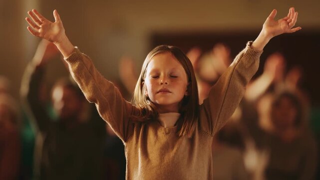 Young girl with closed eyes raising hands in worship or meditation at spiritual gathering