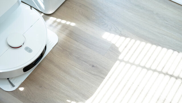 Robotic vacuum cleaner mopping wooden floor with sunlight, smart home appliance using automation for modern lifestyle.