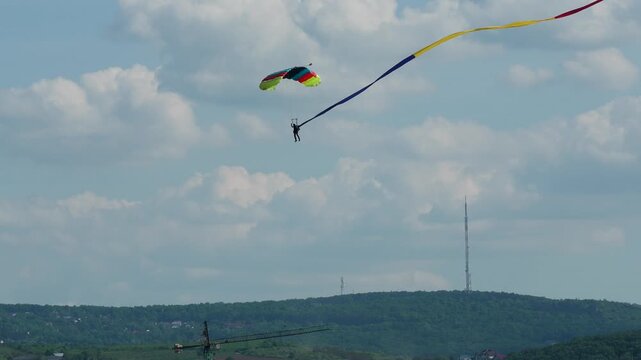 Skydiver descending with colorful parachute and long Romanian flag smoke trail during aviation event in Iasi Romania