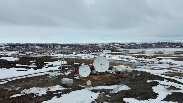 Aerial drone push toward the Telesat satellite dish array and radomes in Iqaluit, Nunavut, during the spring snowmelt.