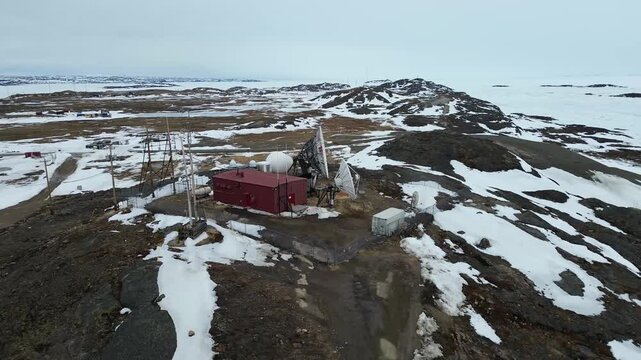 Aerial drone orbit moving left to right around the Telesat satellite earth station in Iqaluit, Nunavut. The city landscape and industrial bulk fuel tank farm are visible in the background.