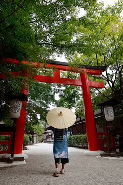 Woman in kimono holding wagasa umbrella standing before red torii gate at Kamigamo shrine, Kyoto, Japan