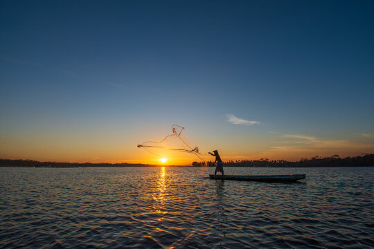 Silhouette of a traditional Indonesian fisherman casting a net from a boat during a golden sunset.