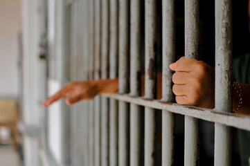 Obraz premium prisoner's hands behind bars with black background
