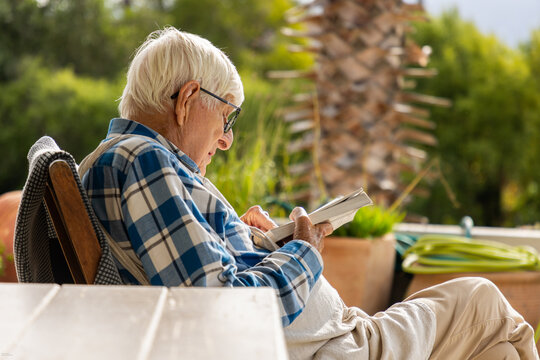 elderly man reading paperback book outdoors