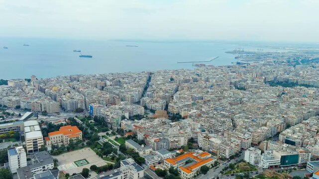Thessaloniki, Greece. the dense cityscape, revealing the historic Rotunda of Galerius amid terracotta rooftops and the Thermaic Gulf stretching to the horizon under hazy summer light. Drone footage