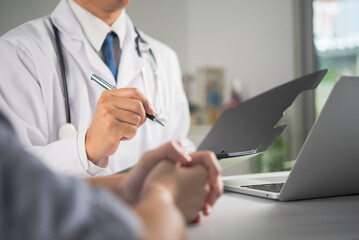 Fototapeta premium Male doctor with stethoscope holding pen and clipboard consulting patient at clinic desk with laptop
