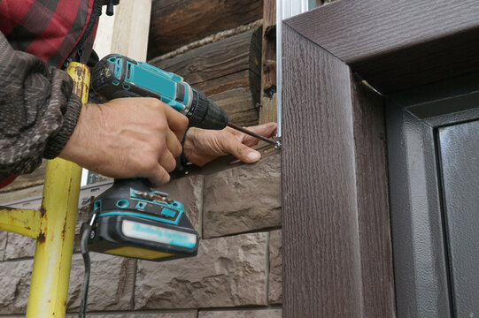 A craftsman screws a siding panel made to look like stone onto the metal frame of a log house.