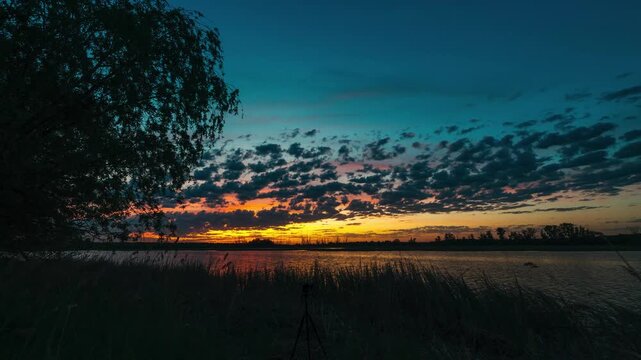 Sunset over a lake with beautiful clouds, timelapse of quickly flying clouds in the sky and the setting sun behind the horizon
