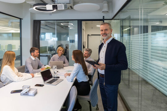 Modern business man in formalwear using digital tablet while standing in the office, colleagues on the background