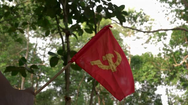 Red hammer and sickle flag gently blows in the wind against a soft out-of-focus jungle background in Laos.
