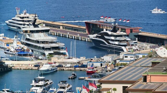 Aerial view of luxury mega yachts docked at the busy harbor in Monaco during a sunny afternoon.