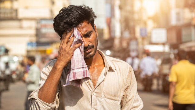 Indian man wiping sweat in extreme summer heatwave on city street