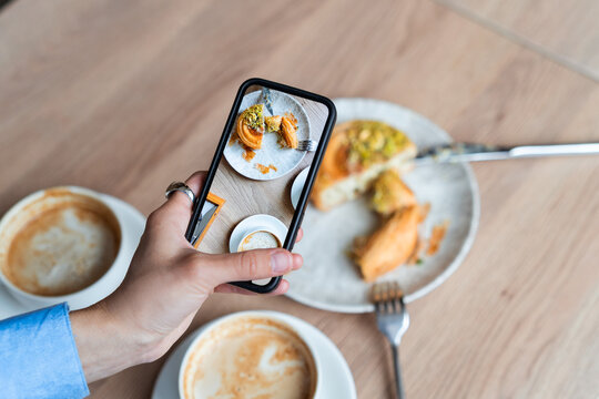 High angle view of a person holding a smartphone and taking a mobile photo of a breakfast table with coffee and pastry