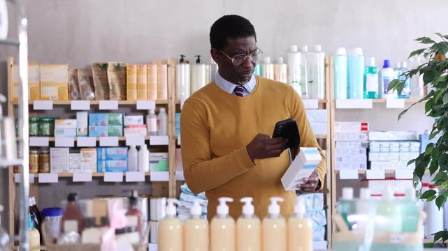 African man in pharmacy scans QR code on cream and uses link to go to manufacturers website. Client learns information about product, reviews and recommendations for use