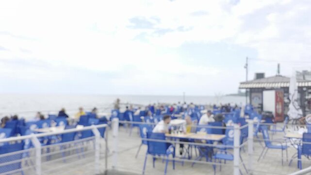 Outdoor seaside cafe terrace with people sitting at tables on a beach promenade.