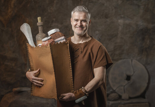 Funny Prehistoric Shopping Concept with Caveman Holding Leather Grocery Bag in a Cave