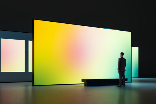 Large illuminated gradient display in modern gallery with a man observing the vibrant screen in a dark interior exhibition space showcasing digital art.